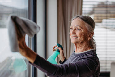 Senior woman cleaning windows, tidy up the house. - HPIF32513