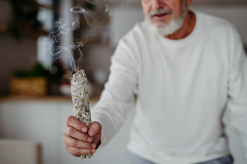 Senior man doing ritual with a sage in his home. - HPIF32517