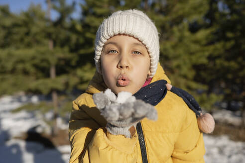 Girl wearing knit hat and blowing on snow in winter - LESF00511