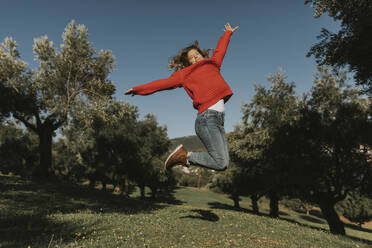 Happy woman jumping near olive trees in field on sunny day - DMGF01136