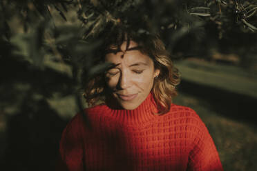 Woman with eyes closed standing under olive tree in field - DMGF01140