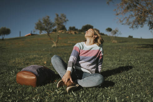 Frau sitzt mit Rucksack und entspannt sich im Gras - DMGF01142