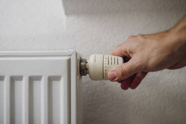 Man adjusting temperature with regulator of radiator in front of wall - HAPF03531