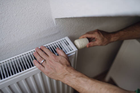 Mann beim Einstellen eines Heizkörpers mit Regler an der Wand - HAPF03535