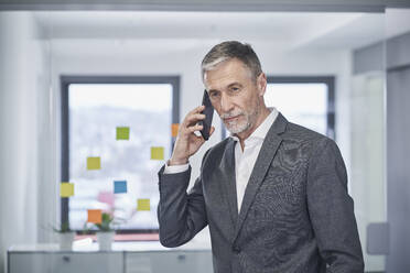 Älterer Geschäftsmann, der im Büro mit seinem Smartphone telefoniert - RORF03596