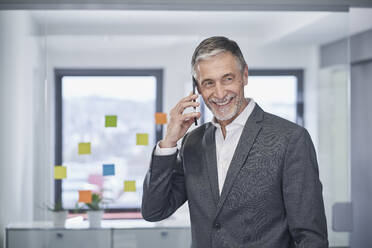 Glücklicher älterer Geschäftsmann, der mit seinem Smartphone im Büro spricht - RORF03597