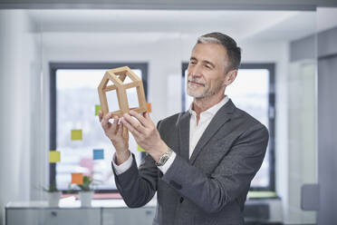 Smiling real estate agent examining model house in office  - RORF03608