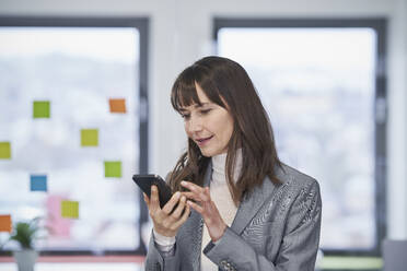 Smiling businesswoman using smart phone in office - RORF03626