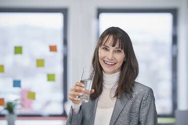 Glückliche reife Geschäftsfrau hält ein Glas Wasser im Büro - RORF03628
