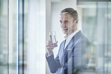 Thoughtful businessman holding glass of water - RORF03635