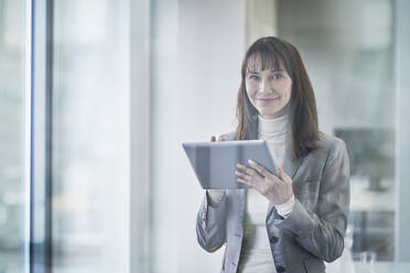 Smiling businesswoman holding tablet PC seen through glass - RORF03642