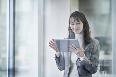 Smiling mature businesswoman using tablet PC seen through glass - RORF03643