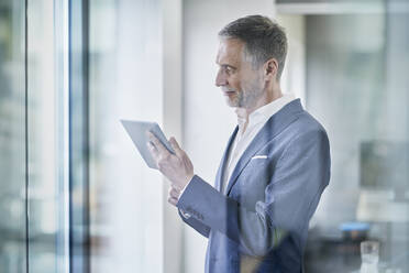 Smiling senior businessman using tablet PC seen through glass - RORF03645