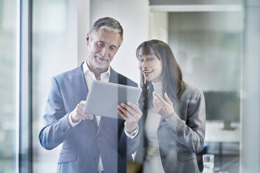 Happy businessman discussing over tablet PC with colleague in office - RORF03648