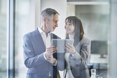 Happy businesswoman and businessman with tablet PC having discussion in office - RORF03650