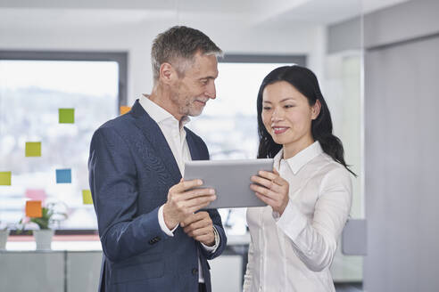 Lächelnde Geschäftsfrau bei einer Diskussion über einen Tablet-PC mit einem Kollegen im Büro - RORF03652