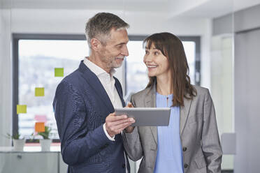 Happy mature businesswoman having discussion with colleague holding tablet PC in office - RORF03654