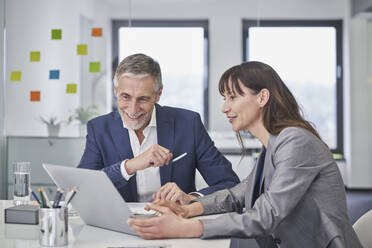 Happy senior businessman discussing with colleague over laptop - RORF03660