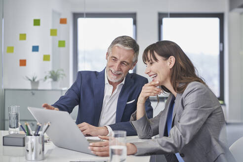 Happy senior businessman discussing with colleague over laptop at desk - RORF03661