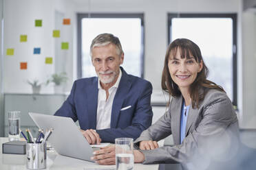 Smiling business people sitting with laptop at desk - RORF03662