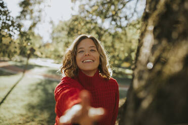 Smiling woman reaching hand in autumn park - DMGF01159