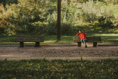 Thoughtful woman sitting on bench in autumn park - DMGF01160