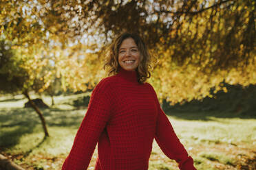 Smiling woman standing under tree in autumn park - DMGF01171