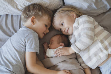 Newborn baby boy sleeping near siblings lying in bed - NDEF01469