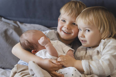 Geschwister halten kleinen Jungen zu Hause im Arm - NDEF01470