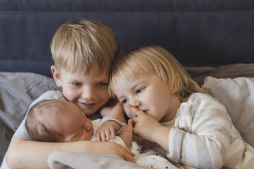 Geschwister halten kleinen Jungen zu Hause im Arm - NDEF01471
