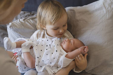 Mother with daughter holding baby boy on bed at home - NDEF01472