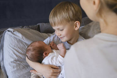 Mother with son holding baby boy on bed at home - NDEF01473