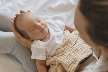 Niedliches neugeborenes Baby schläft zu Hause in den Armen der Mutter - NDEF01488