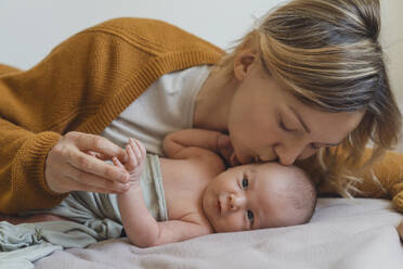 Frau küsst neugeborenen Sohn, der zu Hause auf dem Bett liegt - NDEF01492