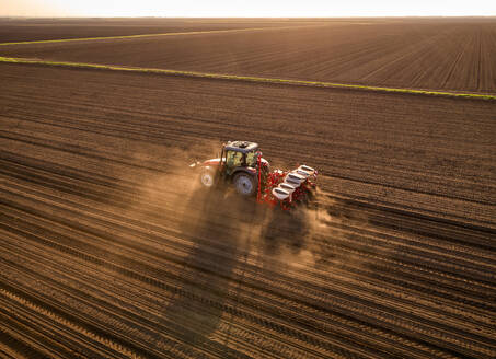 Serbia, Vojvodina Province, Aerial view of tractor sowing seeds in plowed corn field - NOF00818
