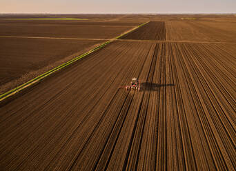 Serbia, Vojvodina Province, Aerial view of tractor sowing seeds in plowed corn field - NOF00820