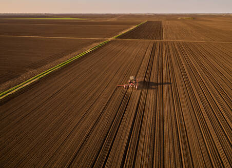 Serbia, Vojvodina Province, Aerial view of tractor sowing seeds in plowed corn field - NOF00820