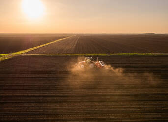 Serbia, Vojvodina Province, Aerial view of tractor sowing seeds at sunset - NOF00823