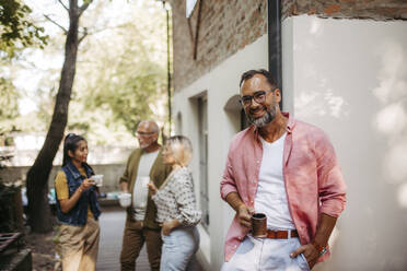 Members of the community have a meeting outdoors, smiling man drinking coffee - HAPF03583