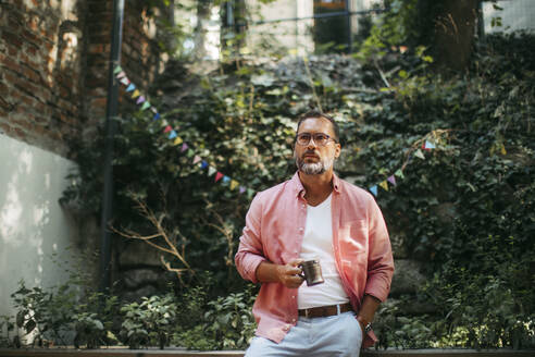 Pensive man drinking coffee in community garden - HAPF03585