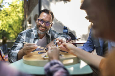 Freunde sitzen im Garten und haben Spaß beim Essen von Sushi mit Stäbchen - HAPF03652