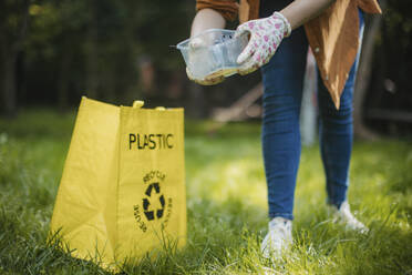 Woman putting plastic waste recycling bag at parl - HAPF03694