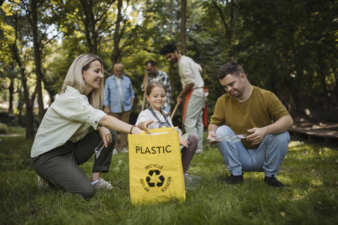 Sozial integrative Gruppe von Freiwilligen, die Plastikabfälle in Recyclingsäcke füllen - HAPF03697