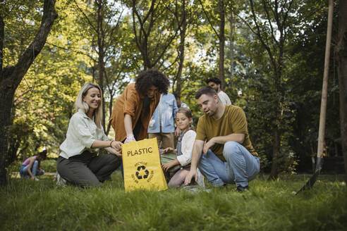 Socially inclusive group of volunteers putting plastic waste in recycling bag - HAPF03699