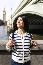 Lächelnde Frau steht mit geschlossenen Augen an einem sonnigen Tag in London - WPEF07957