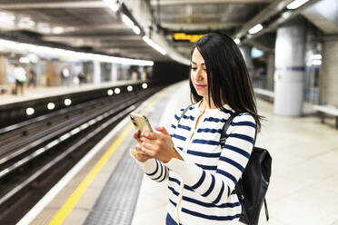 Lächelnde Frau mit Smartphone in der U-Bahn-Station - WPEF07961