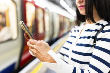 Woman using smart phone near subway at station - WPEF07962