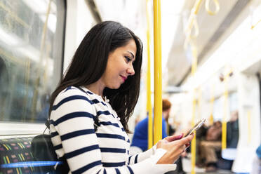 Lächelnde Frau mit Smartphone in der U-Bahn - WPEF07968