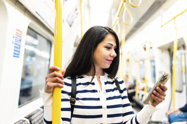 Lächelnde Frau, die in der U-Bahn ein Mobiltelefon benutzt - WPEF07972