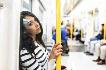 Kontemplative Frau, die einen Stock hält und in der U-Bahn fährt - WPEF07974